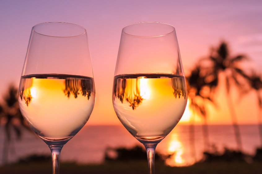 two wine glasses with white wine and sunset on the background
